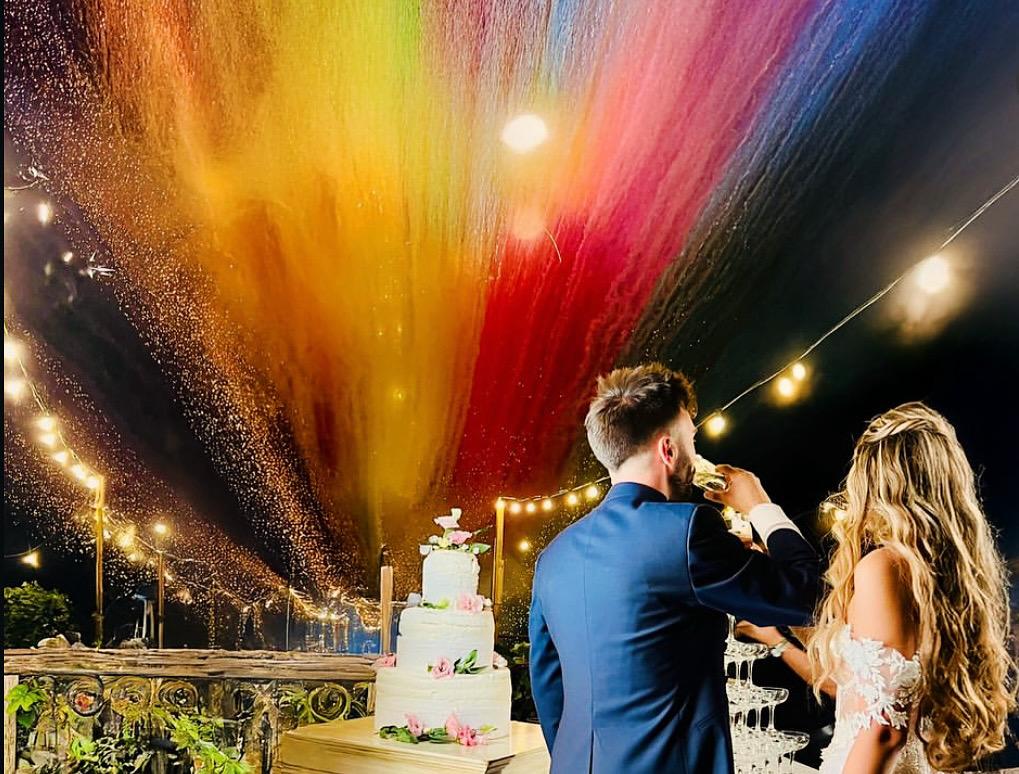 Coppia durante il brindisi davanti alla torta con grande effetto di fumo colorato nel cielo.